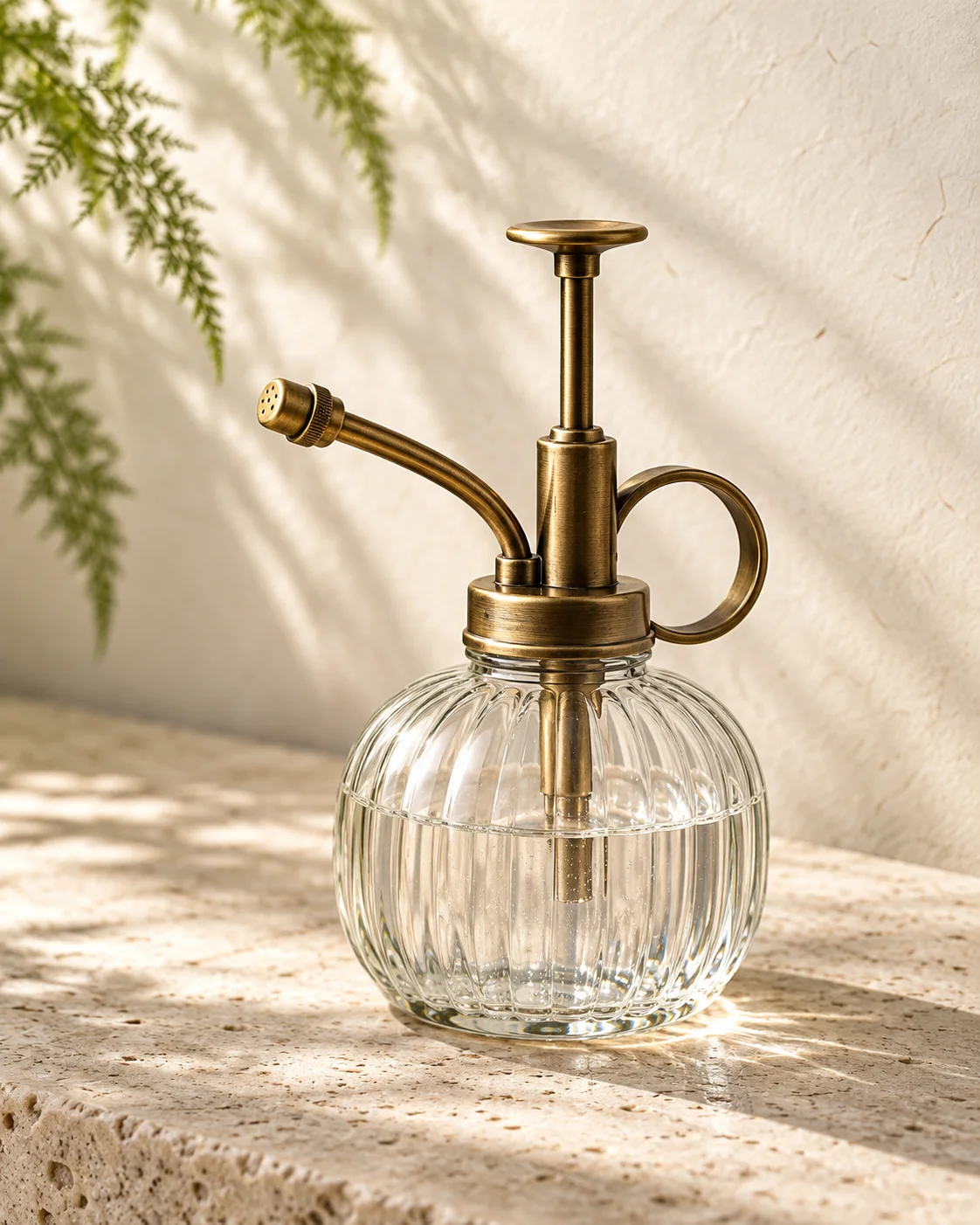A ribbed glass plant mister with a brass-colored pump.